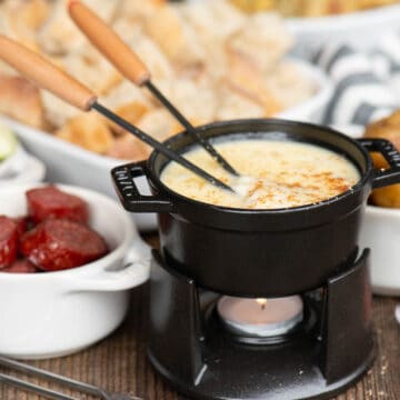small black dish with cheese fondue and cheese fondue dippers.