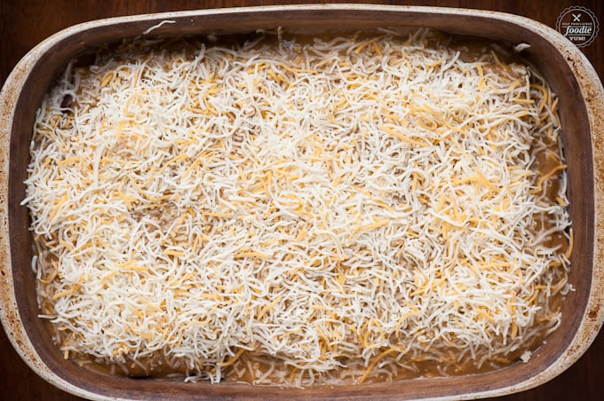 shredded cheese in casserole dish while making Green Chile Chicken Lasagna