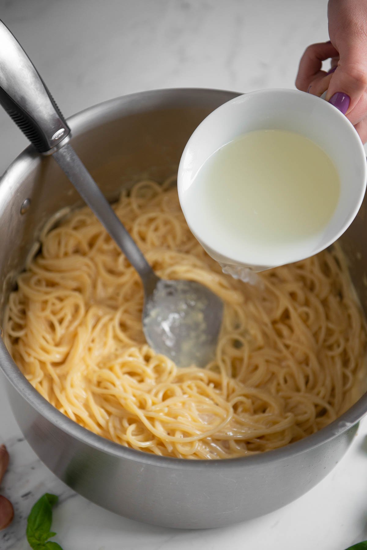 adding salted pasta water to carbonara pasta to thin sauce.