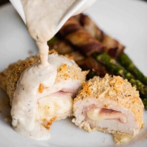 homemade chicken cordon bleu cut in half with cream sauce getting poured