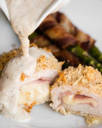 homemade chicken cordon bleu cut in half with cream sauce getting poured