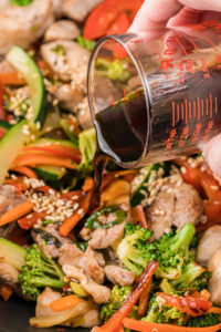 pouring sauce over stir fried chicken and vegetables.