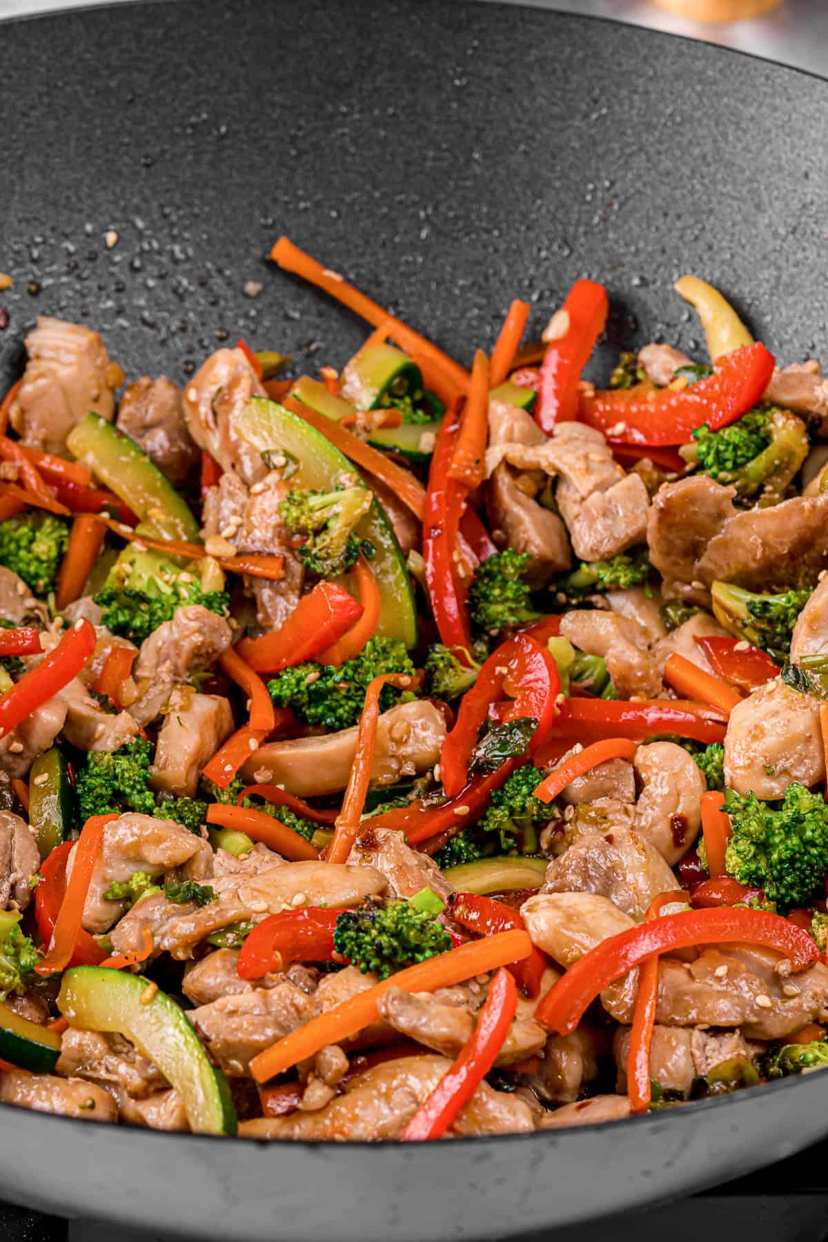 chicken stir fry with peppers, onions, broccoli and zucchini in wok pan.