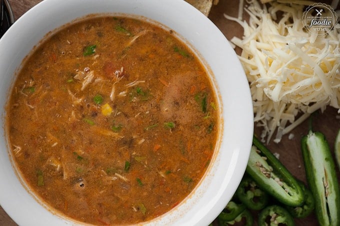 bowl of chicken and bean soup with shredded cheese and sliced jalapeno