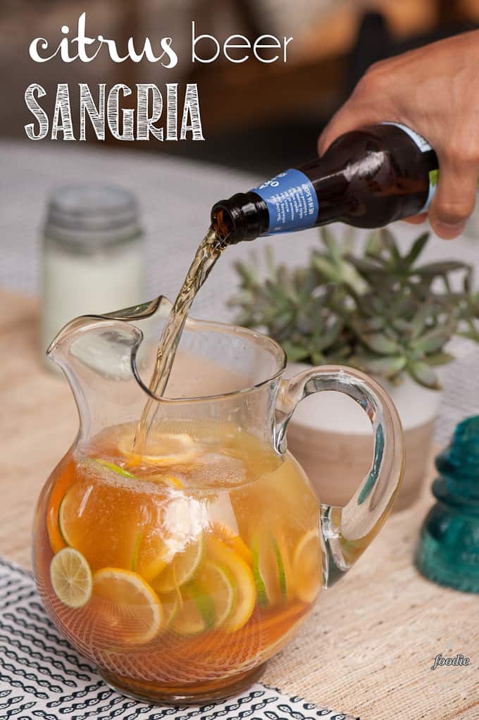 hard cider pouring into pitcher with sliced citrus