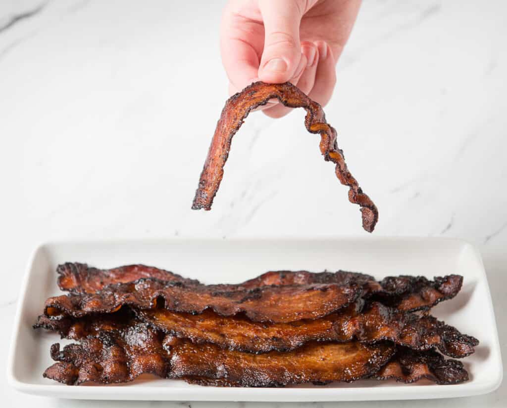 hand holding a perfect slice of oven baked chewy bacon
