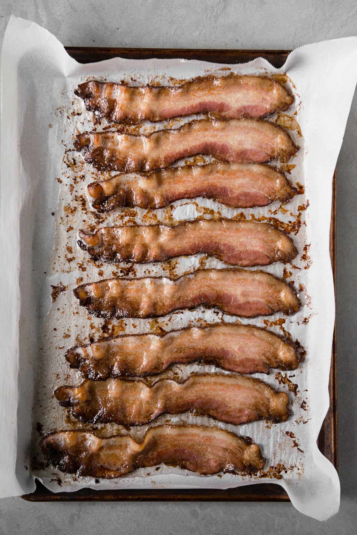 partially cooked bacon slices on parchment lined baking sheet