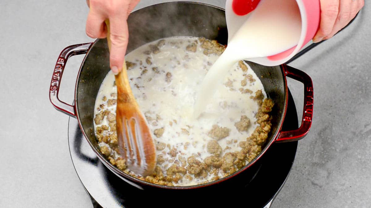 Adding milk to crumbly cooked breakfast sausage coated in roux to make a creamy sausage gravy for biscuits and gravy.