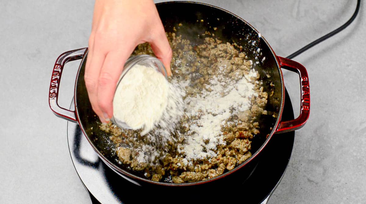 adding flour to cooked ground breakfast sausage.