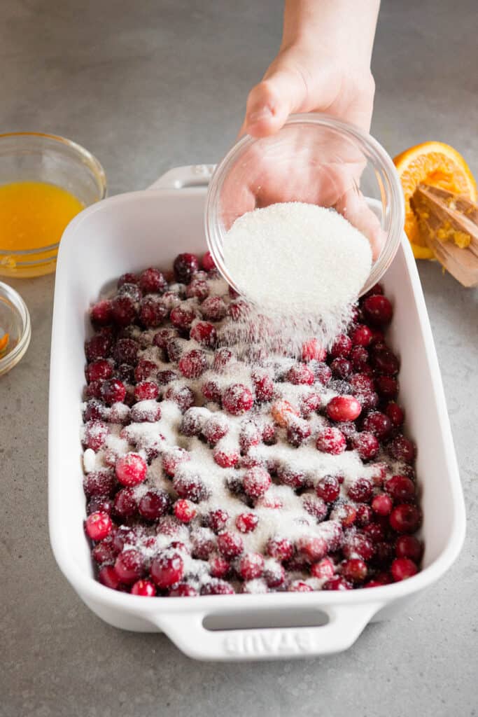 sprinkling sugar on fresh cranberries in casserole dish