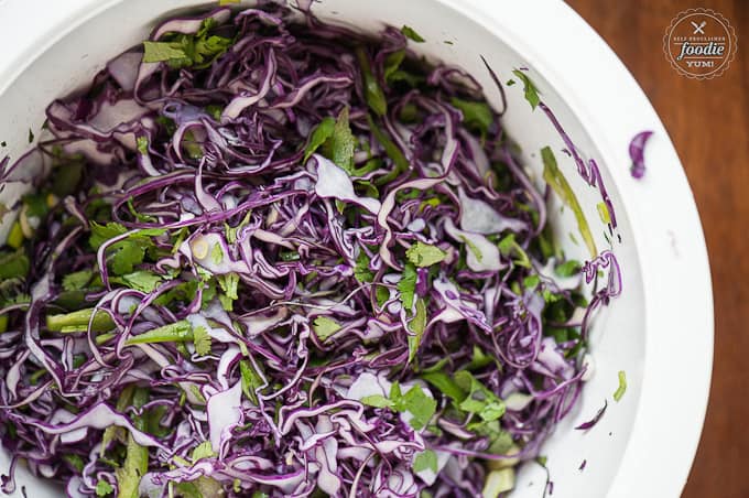 homemade cole slaw ingredients in white bowl including shredded cabbage and cilantro