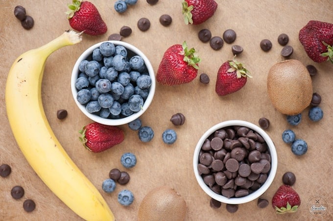 blueberries, strawberries, kiwi, a banana, and chocolate chips on a wooden surface