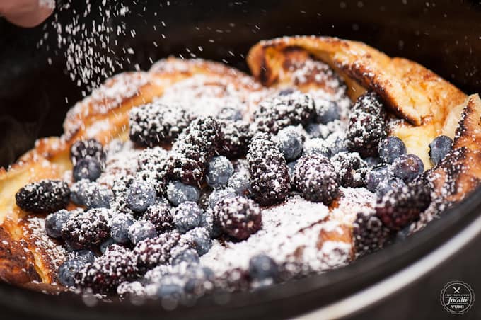 powdered sugar being poured on a dutch oven dutch baby