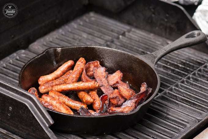 A tray of sausages and bacon cooking on a grill