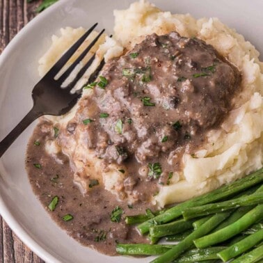 salisbury steak on top of mashed potatoes with green beans and gravy.