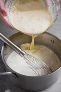 pouring tempered egg mixture into pan for homemade eggnog recipe