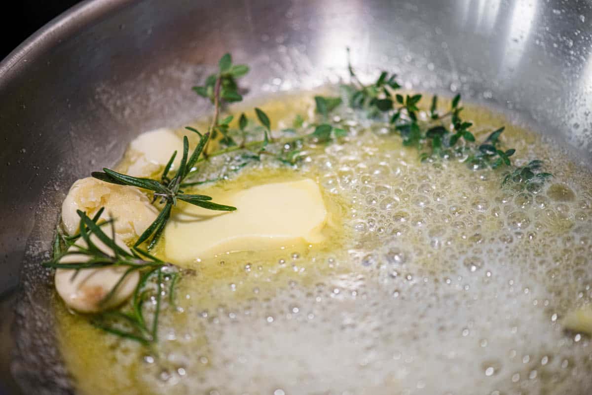 infusing garlic and herbs in butter in pan