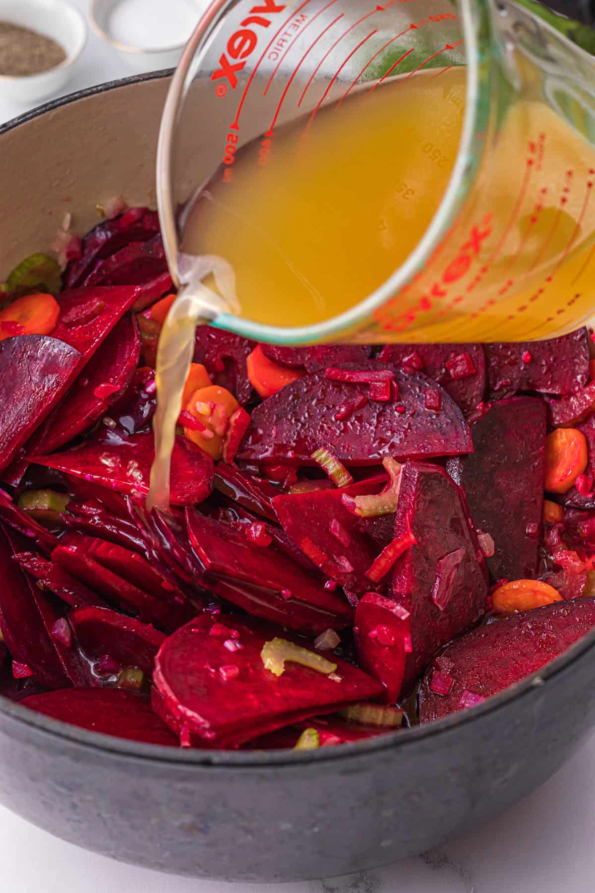 adding chicken broth to vegetables for fresh beet soup recipe.