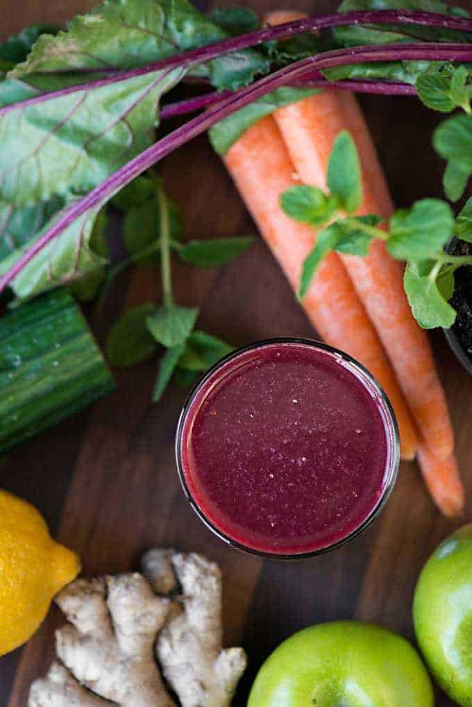 a glass of fresh pressed juice with vegetables in the background