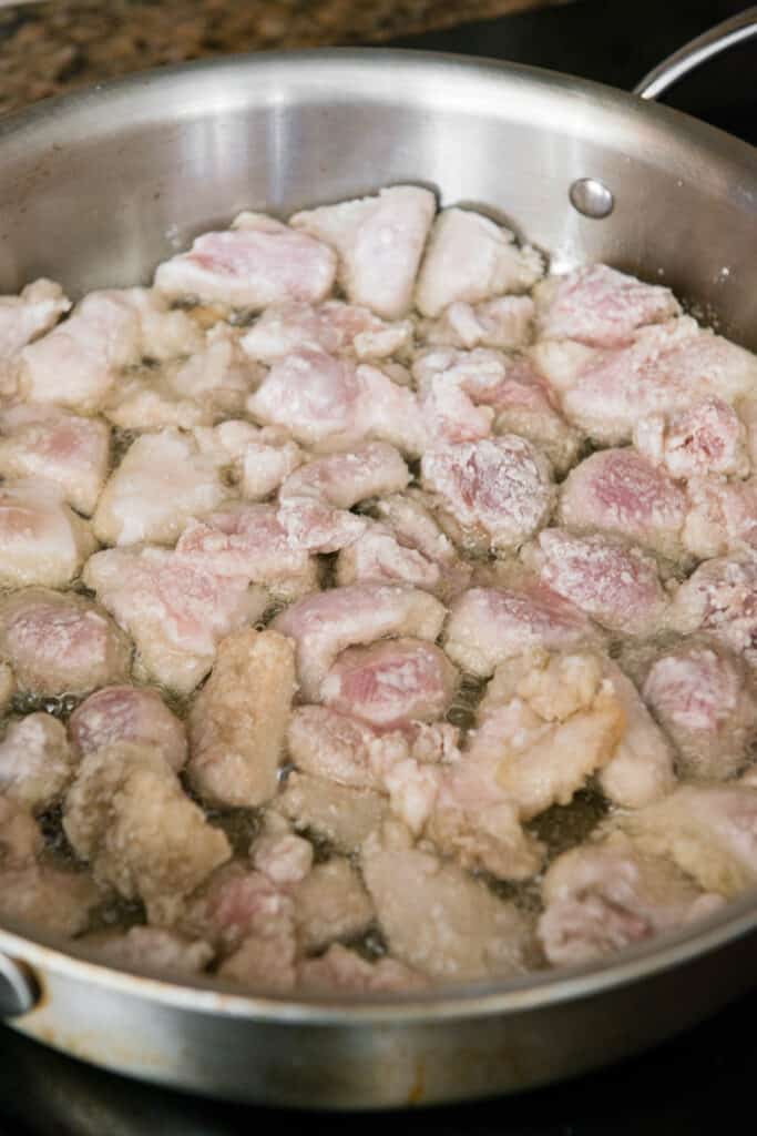 chicken thigh pieces coated in corn starch cooking in oil