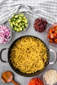 Cooked fusilli pasta in pot with ingredients to make Greek pasta salad.