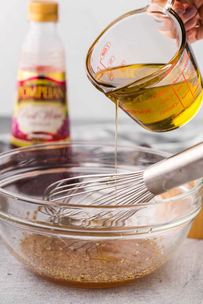 Adding olive oil to vinaigrette for Greek pasta salad recipe.