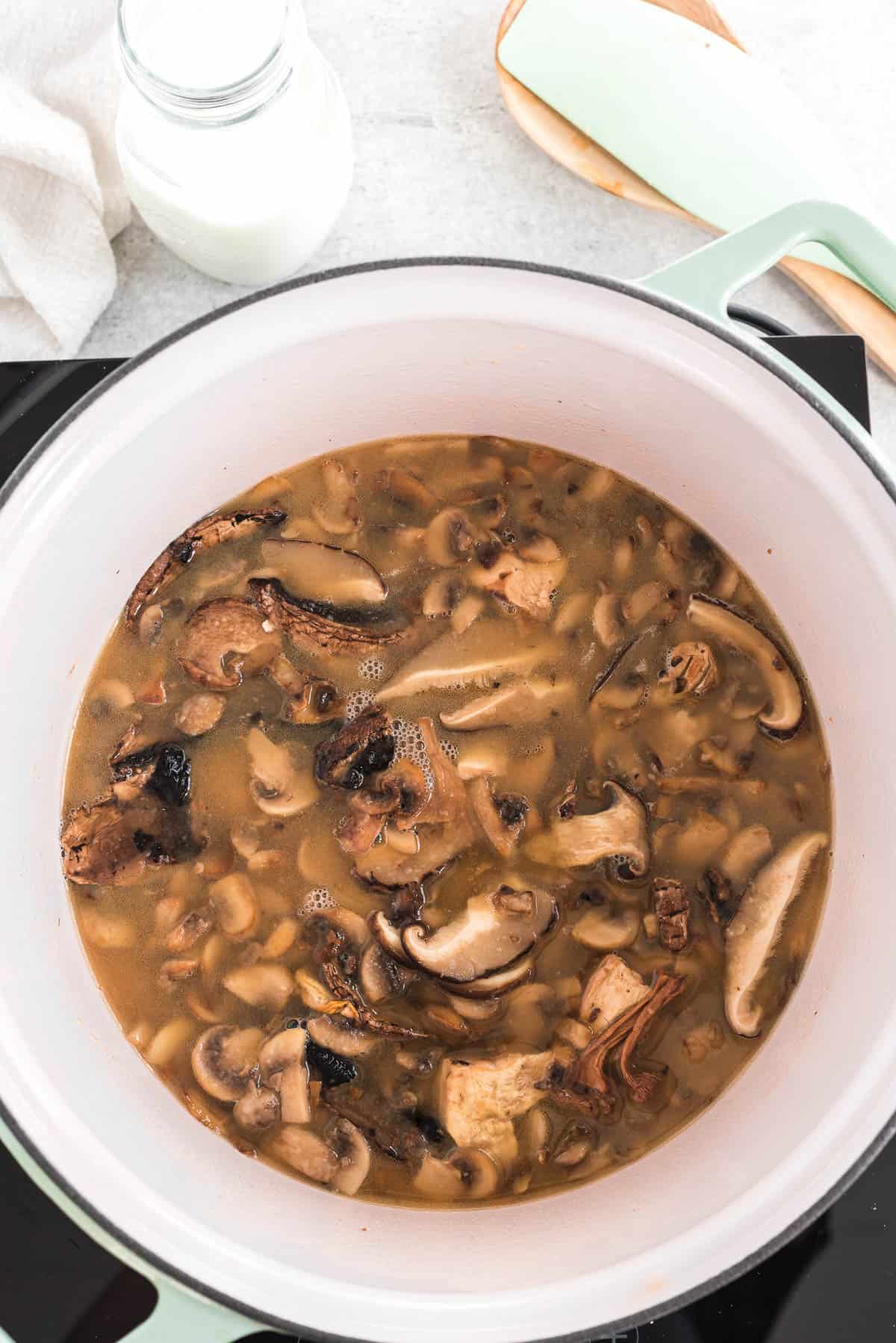 adding chicken broth to sauteed mushrooms for mushroom gravy.