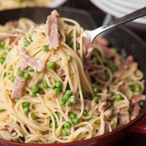 scooping homemade Pasta Carbonara with Ham and Pea out of pot
