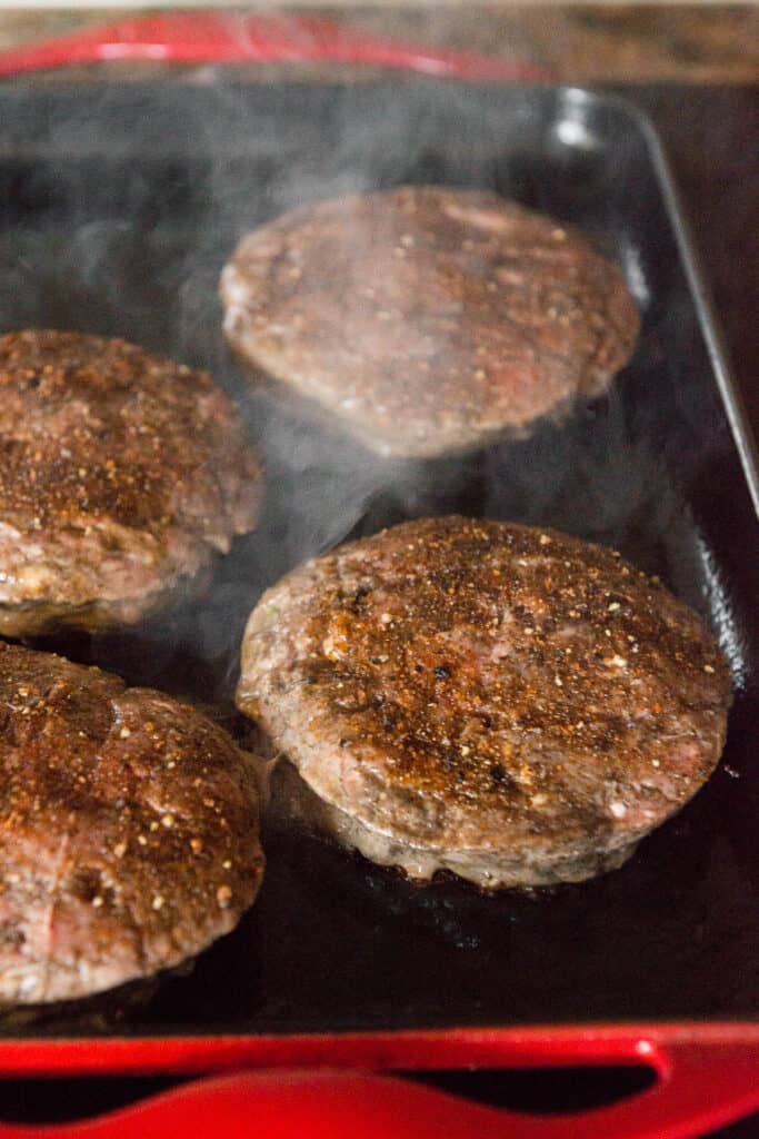 seasoned hamburger patties cooking on griddle