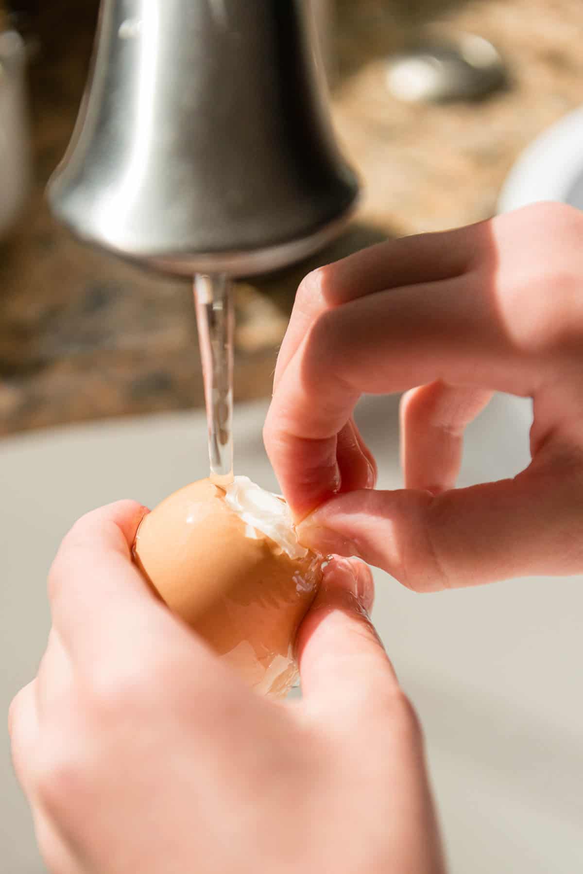 peeling hard boiled egg under running water.