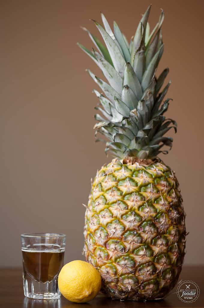 A pineapple sitting on a table with whiskey in a glass