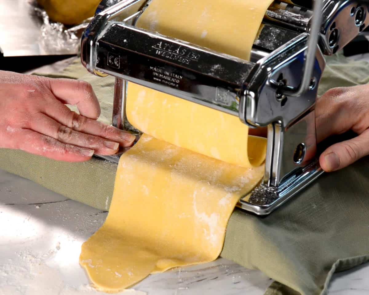 rolling large sheet of pasta dough through hand roller.