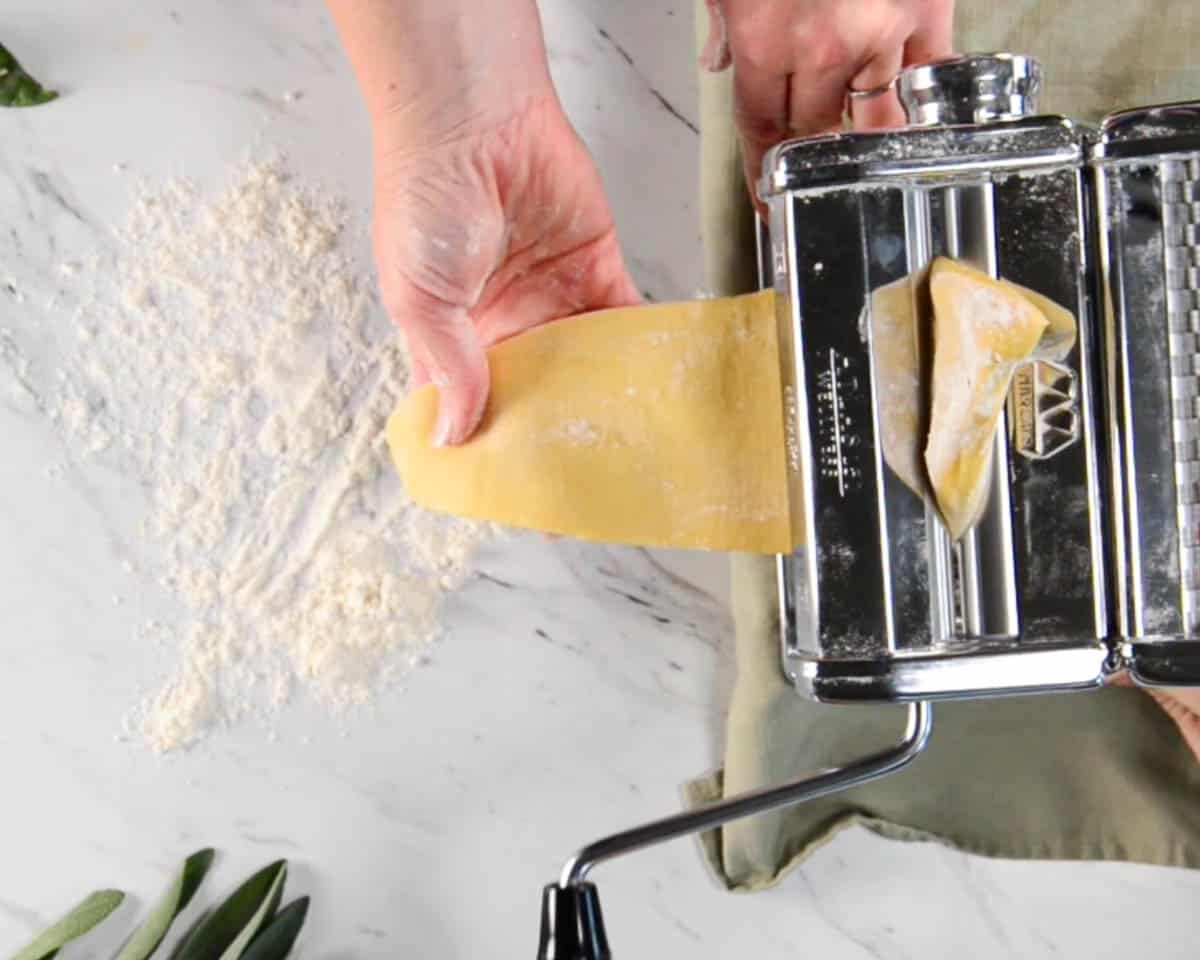 rolling sheets of pasta through a roller.