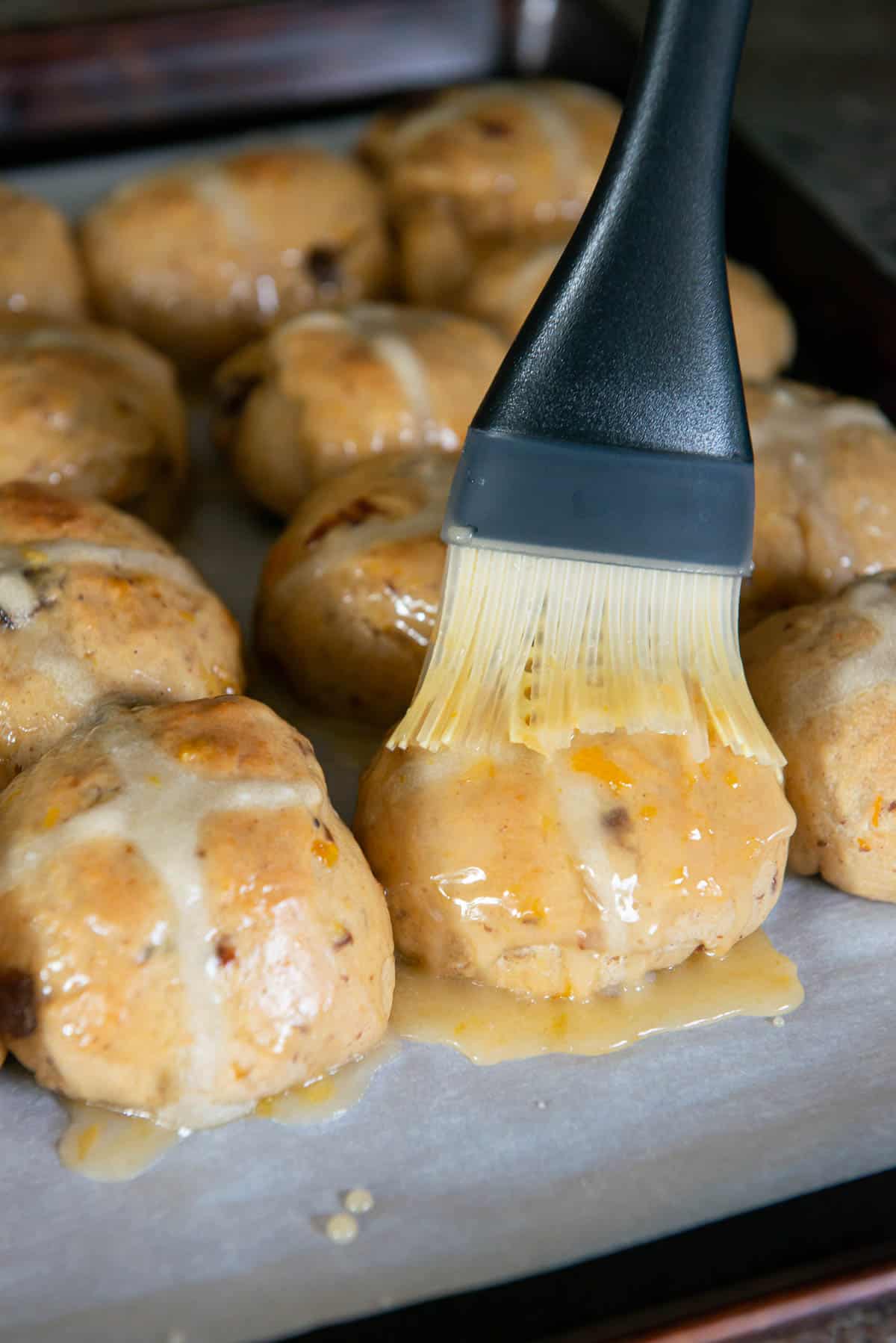brushing orange glaze on warm hot cross buns.