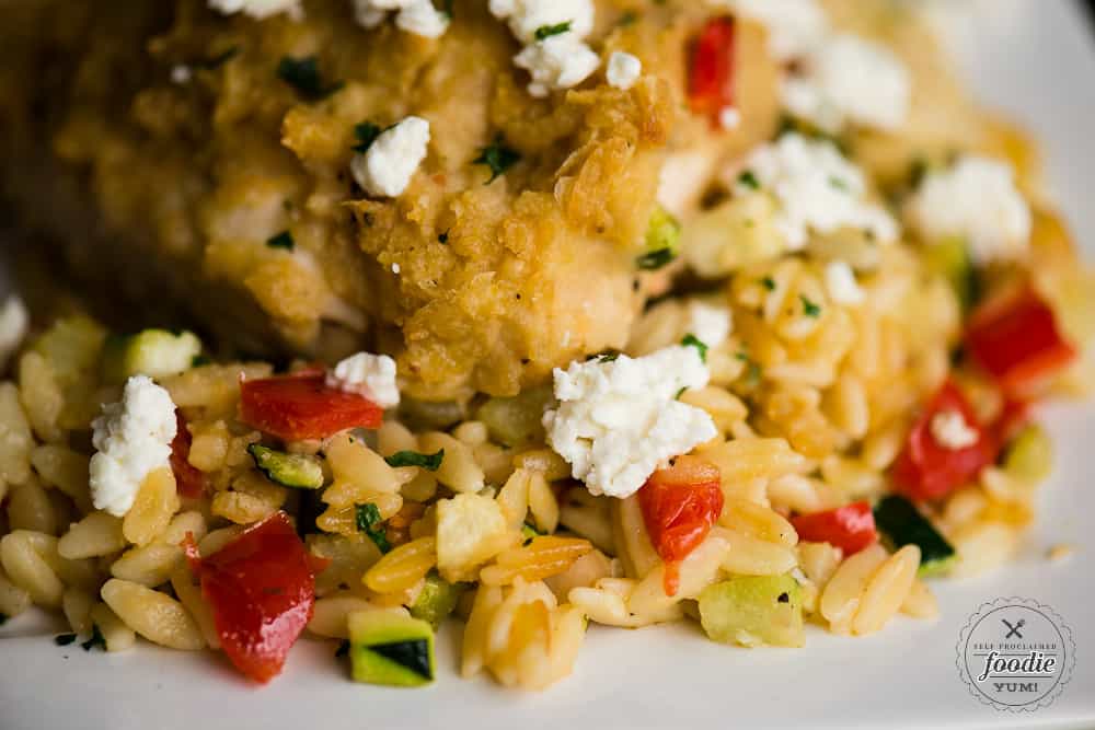 A close up of hummus baked chicken with feta and vegetable orzo