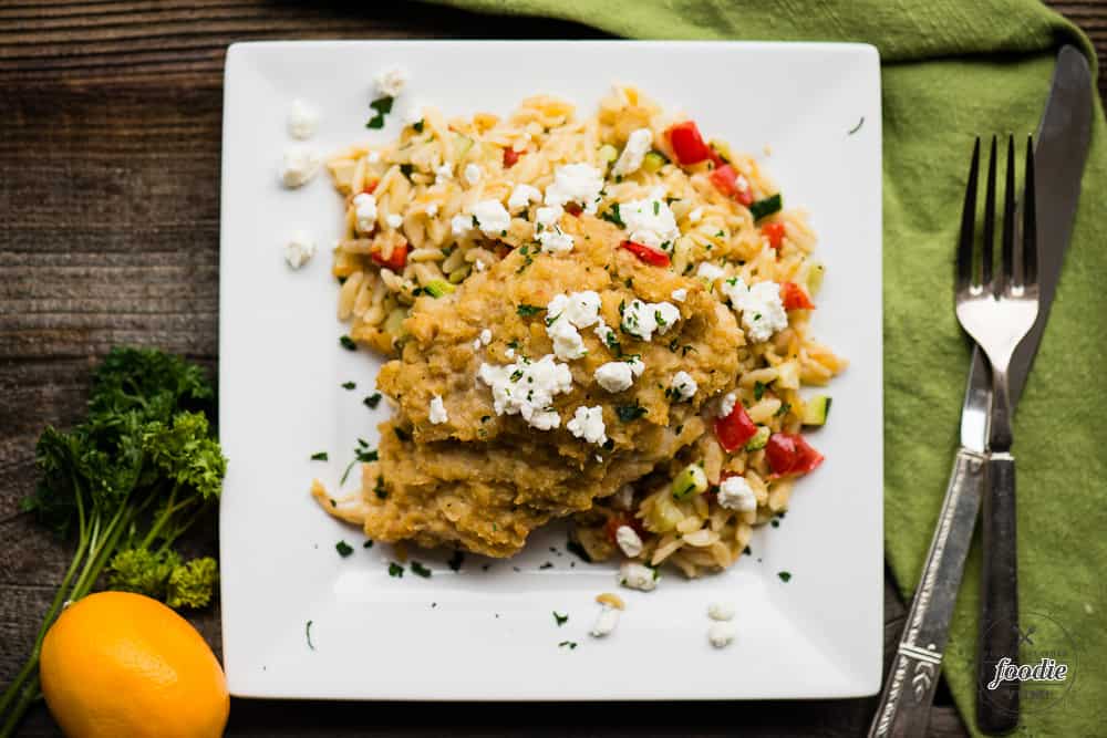 A plate of food with hummus baked chicken with feta and vegetable orzo