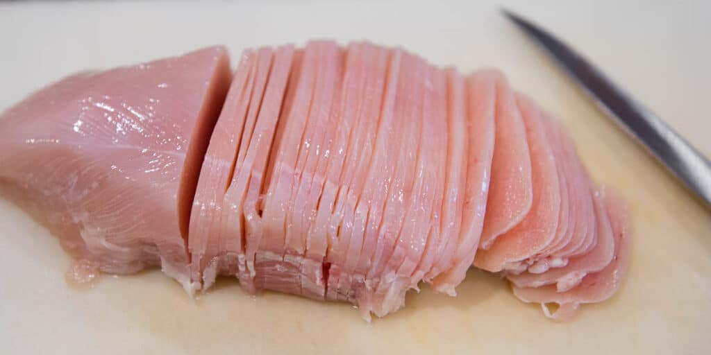 very thinly sliced raw chicken breast on cutting board