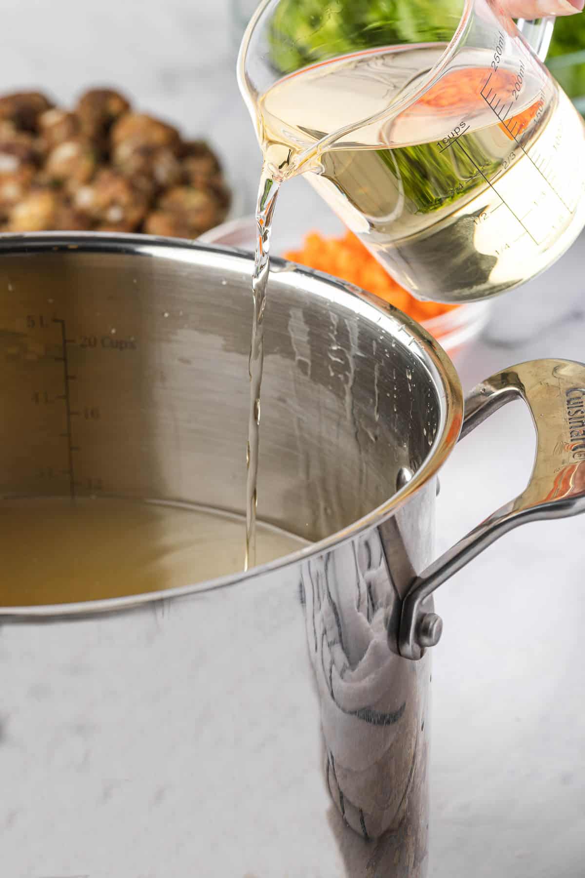 Pouring white wine into pot for soup recipe.