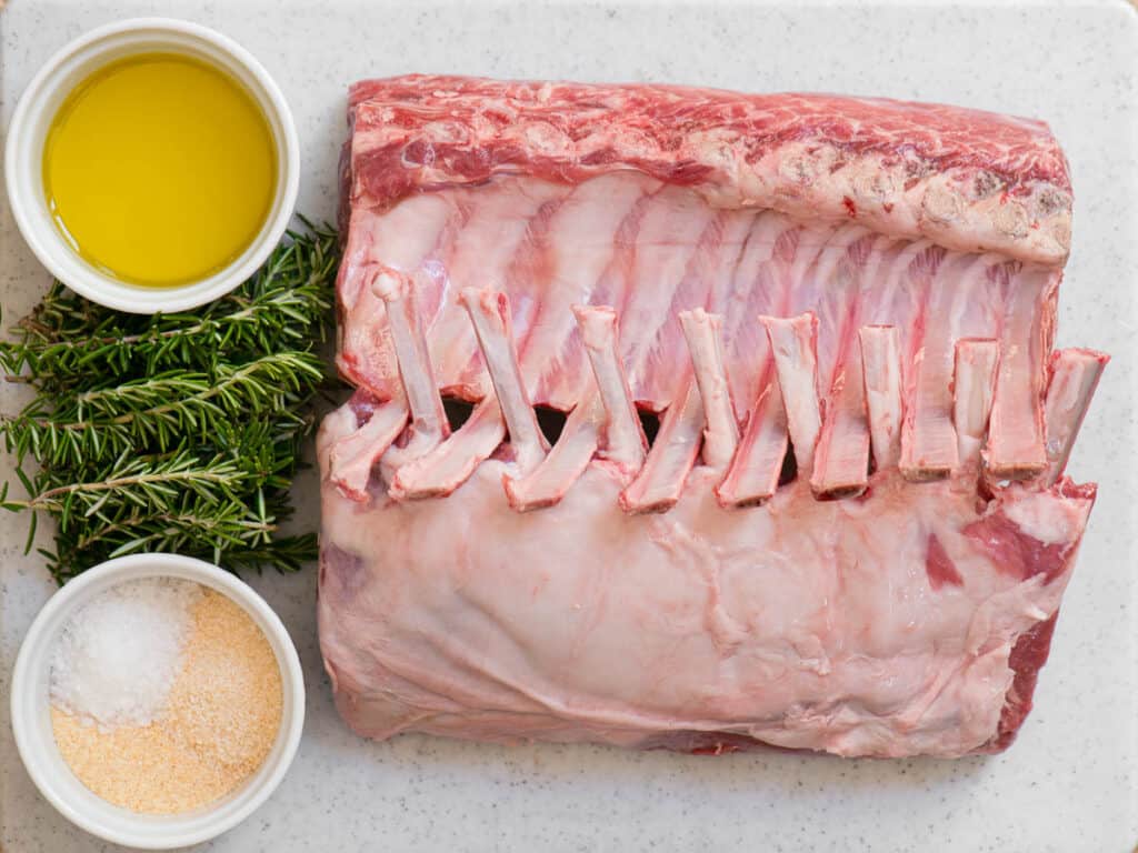 two raw racks of lamb with oil, herbs, and seasonings