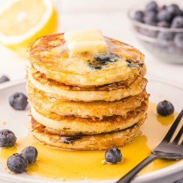 stack of homemade lemon blueberry pancakes with butter and syrup.
