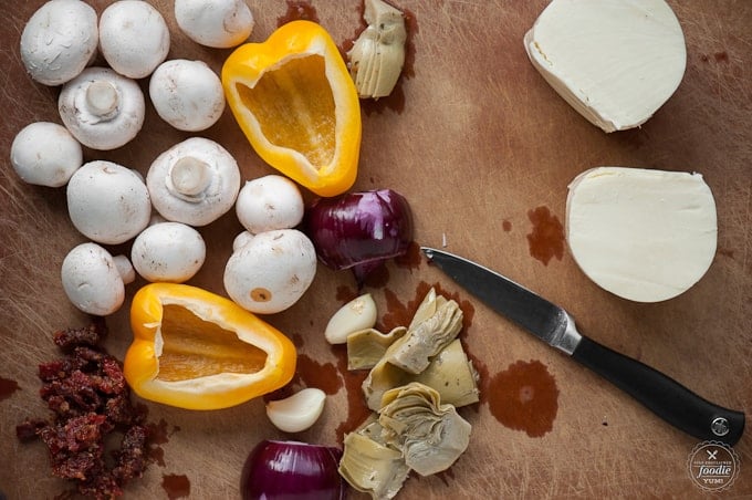 mushrooms, cheese, peppers, onions,and artichoke sitting on a cutting board