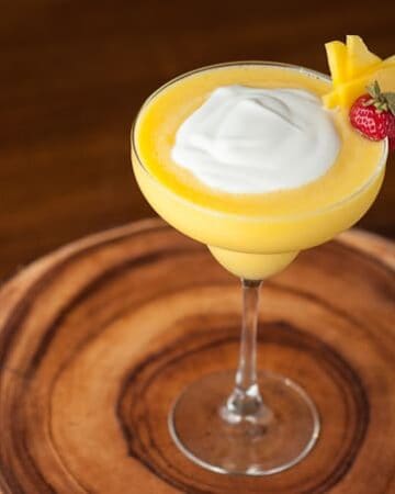 A margarita glass with a Mango Coconut daiquiri with a cream topping and garnish