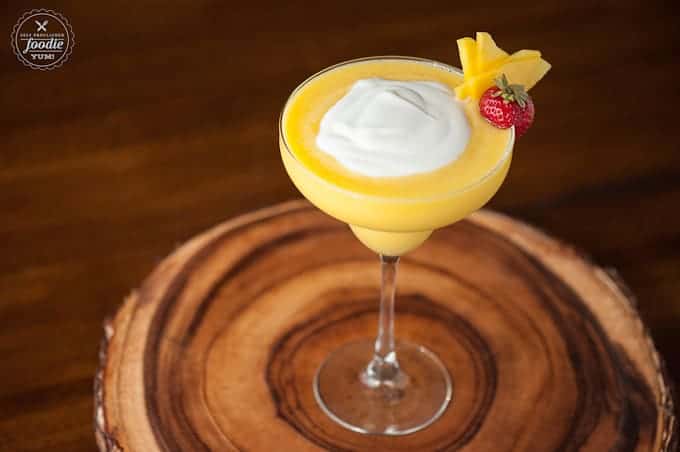 A margarita glass with a Mango Coconut daiquiri with a cream topping and garnish