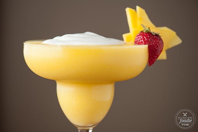 a close up of a blended coconut mango daiquiri with strawberry garnish