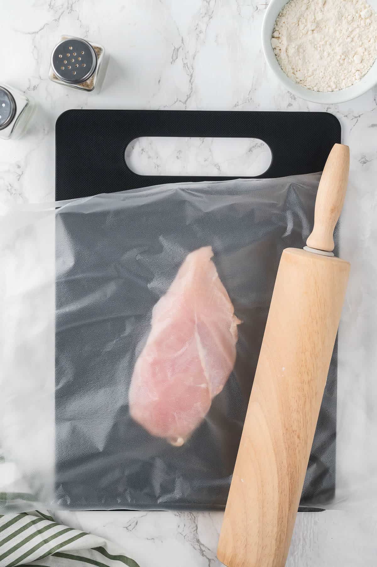 rolling a chicken breast to make it thinner.