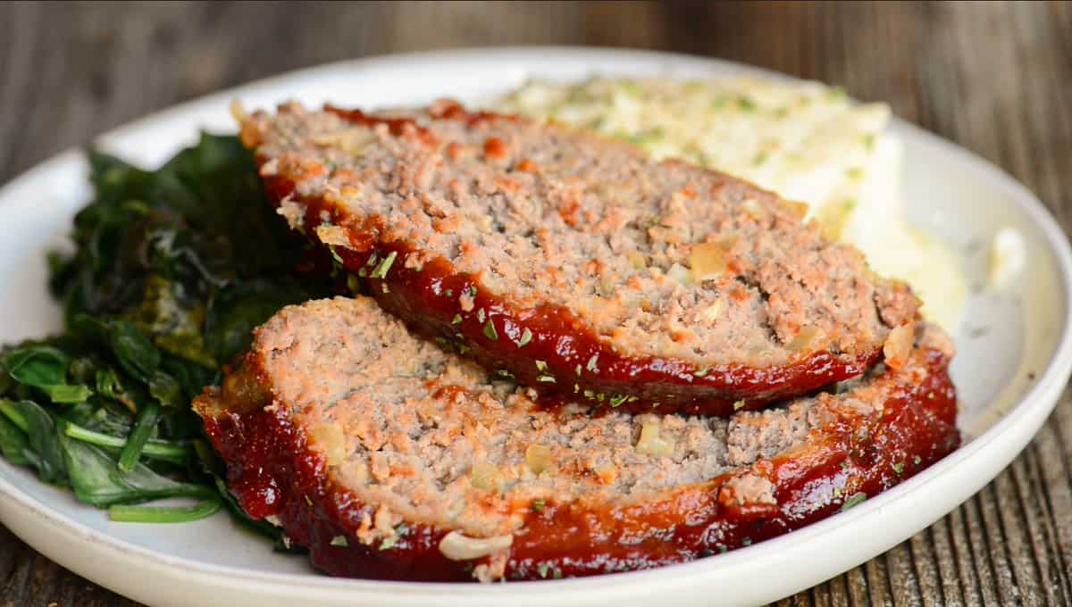 two slices of meatloaf on plate with mashed potatoes and spinach.