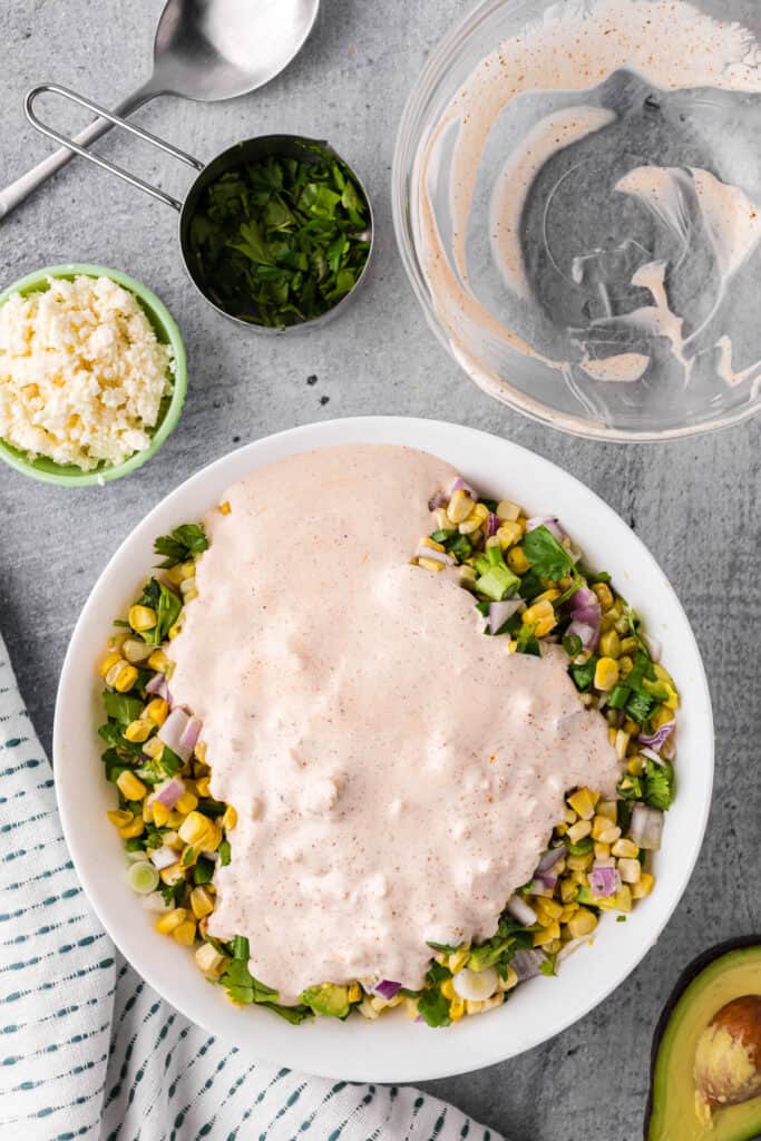 Adding dressing to Mexican street corn salad.