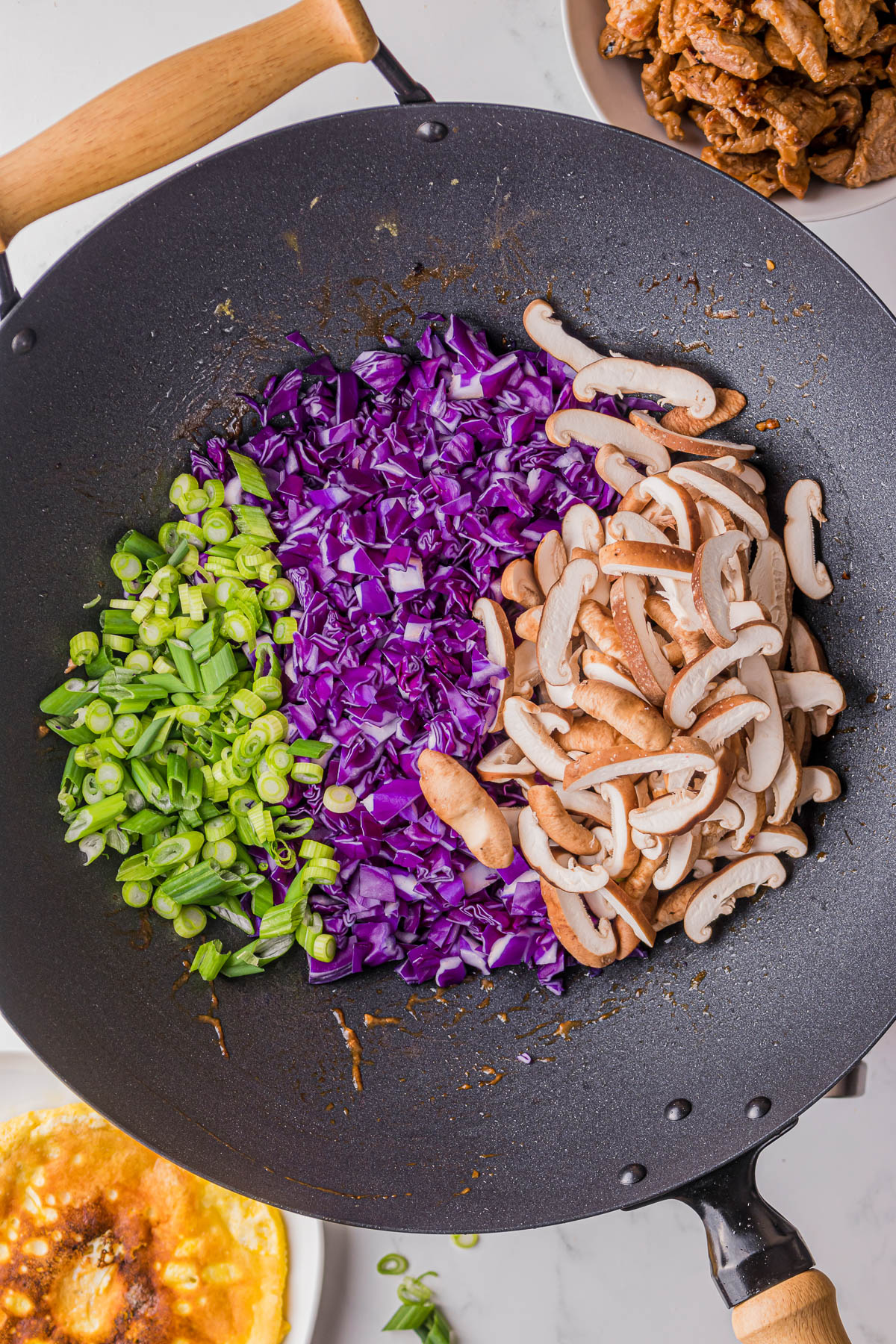 cooking chopped green onions, purple cabbage, and mushrooms in a wok pan.