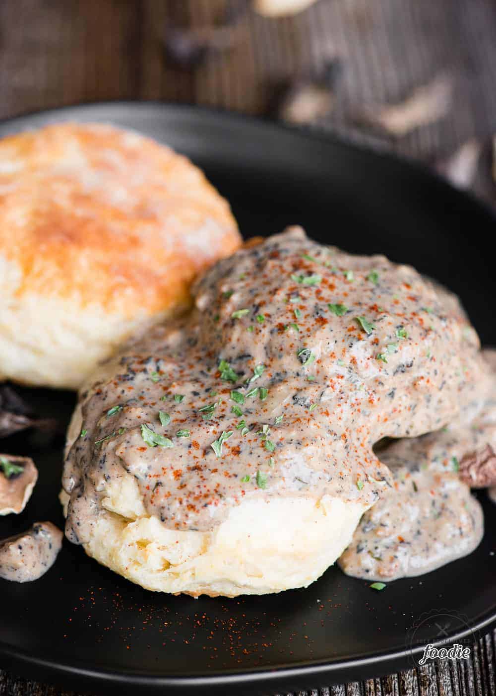 black plate with two homemade buttermilk biscuits topped with vegetarian country mushroom gravy