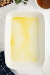greasing a white casserole dish with butter.
